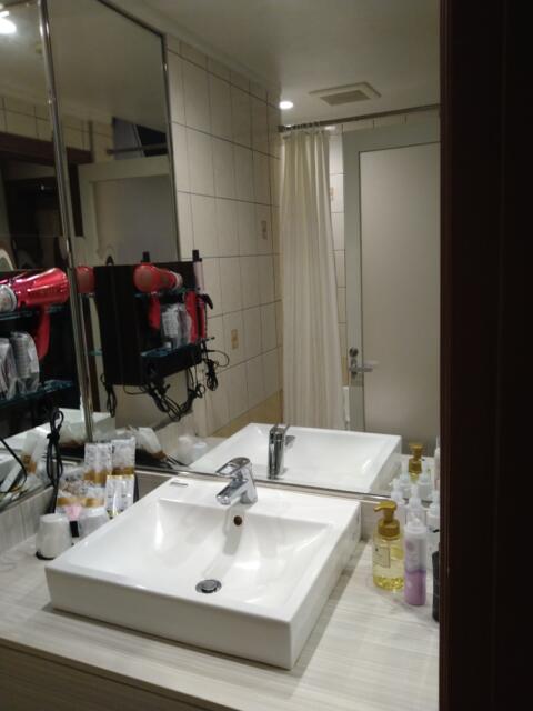 HOTEL CUE厚木(厚木市/ラブホテル)の写真『405号室 洗面所。すぐ向かいにバスタブがあるが、鏡に写っている扉はバスルームの為のものではなく洗面所に入る為のもので、シャワーカーテンの奥がすぐバスタブ。洗い場が無い。これだけ広いホテルなのに何故ユニットバスのような造りにしたのか謎である…』by なめろう